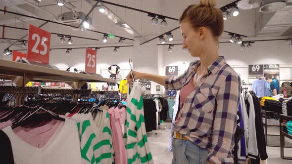 happy woman chooses clothes in form of blouse and in shopping center