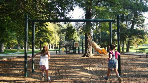 Two little girls run up to swing-set and start swinging