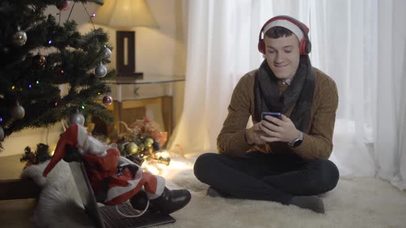 Carefree Young Man in Headphones Listening To Music From Smartphone Playlist and Dancing Sitting at