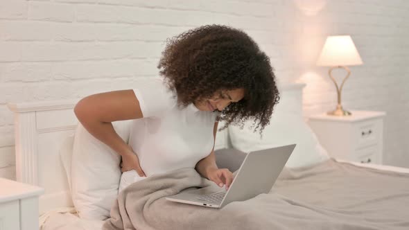 Young African Woman with Laptop Having Back Pain in Bed