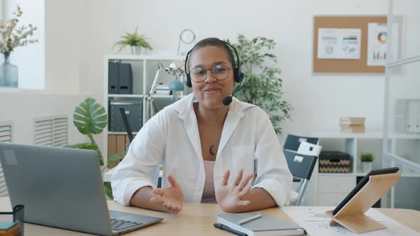 Portrait of AfroAmerican Businesswoman in Headphones Talking and Gesturing Looking at Camera