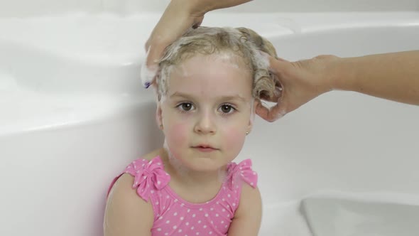 Cute Blonde Girl Takes a Bath in Swimwear. Little Child Washes Her Head