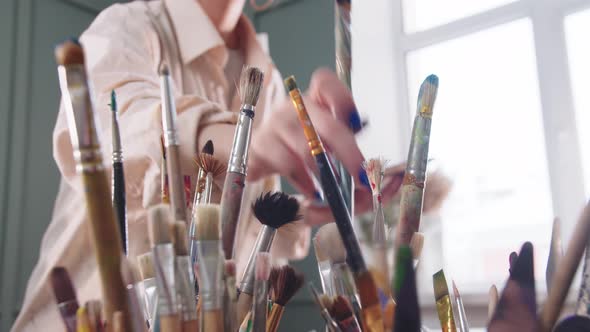 A Woman Artist in a Paintstained Shirt Changes a Brush