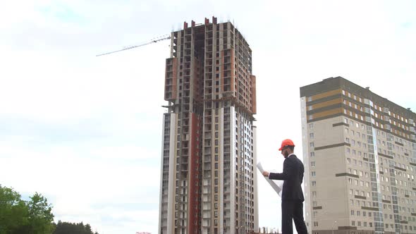 Architect Looking at Building Plans with New Construction