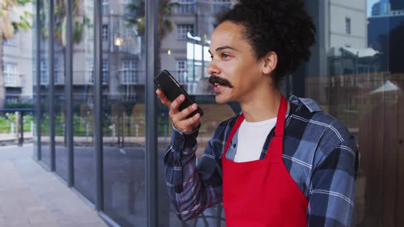 Mixed race male barista with moustache wearing an apron talking on smartphone