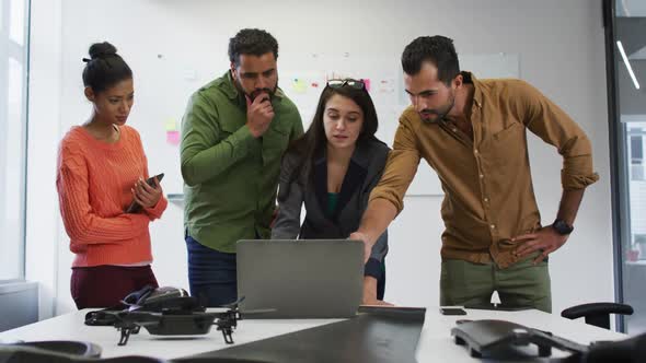 Diverse group of work colleagues looking at laptop and discussing in meeting room