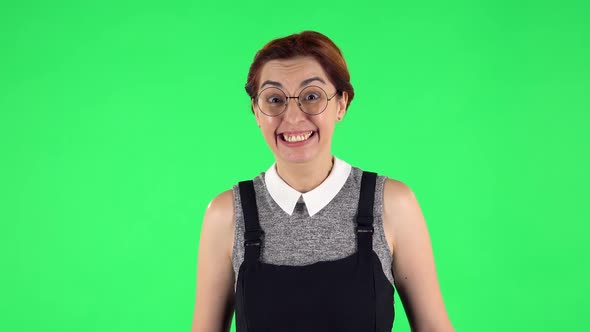 Portrait of Funny Girl in Round Glasses Is Smiling Broadly and Winking . Green Screen