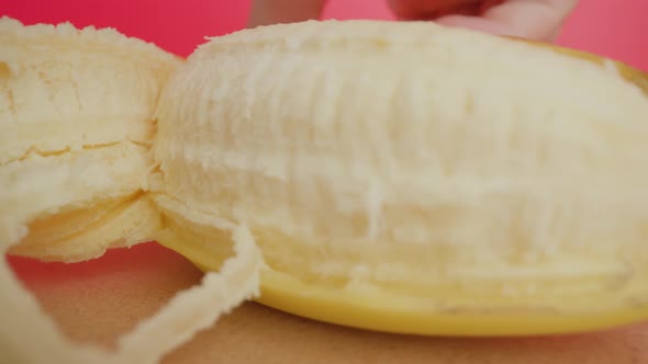 Man Peels Yellow Banana Skin Slowly Against Pink Wall