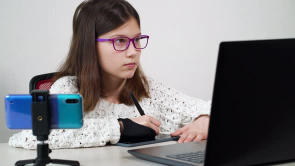 Creative girl drawing on graphic tablet and watching online course on smartphone