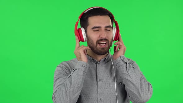 Portrait of Brunette Guy Is Dancing and Enjoying Music in Big Red Headphones. Green Screen