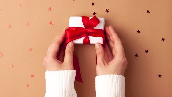 Human hands in white sweater puts and take away a white paper gift with a red satin ribbon bow