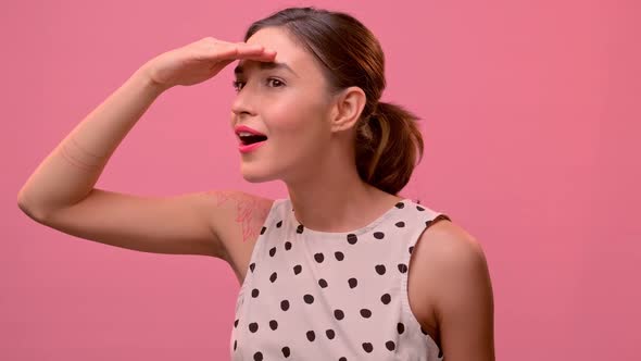 Woman Joyfully and Anxiously Looking for Someone on a Background of a Pink Wall.