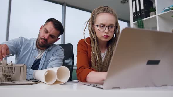 Woman with Dreadlocks Working on Laptop while Her Confident Purposeful Bearded Colleague Taking