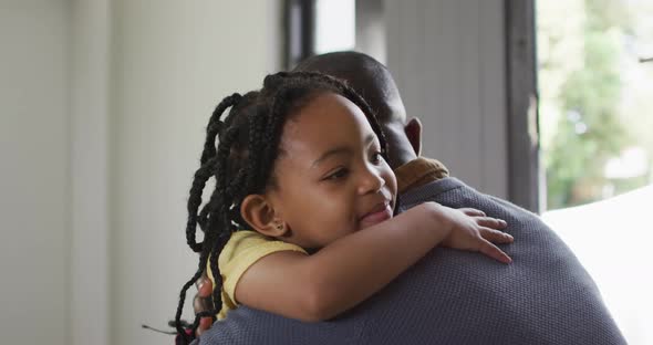 Happy african american daughter and father hugging on sofa