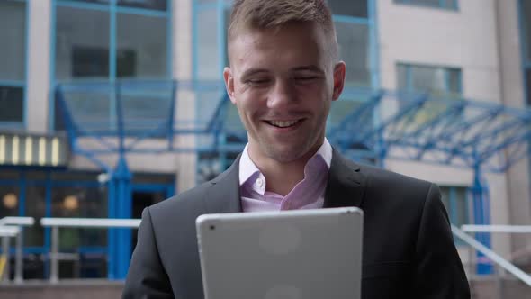 Happy Young Male Manager Standing Outdoors at Business Center Surfing Internet on Tablet