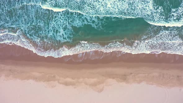 Aerial view of waves crash to shore at sunset