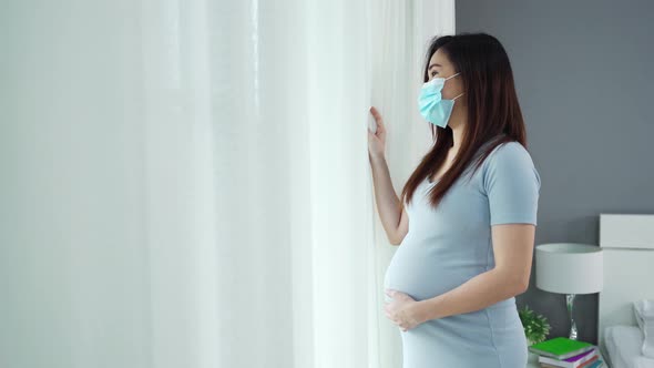 pregnant woman in medical mask and looking through window in a bedroom