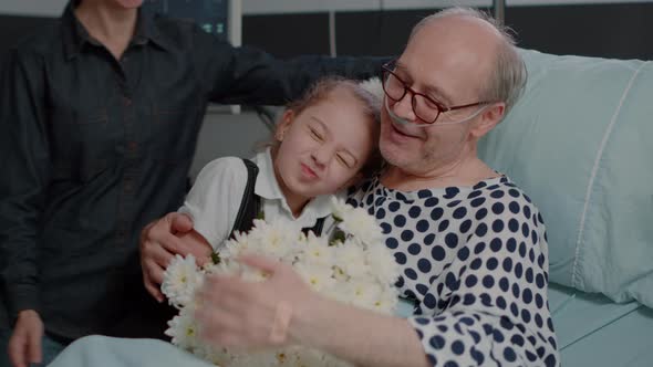 Close Up of Little Girl Bringing Flowers to Grandpa in Hospital Ward Bed