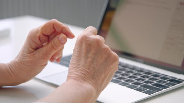 Old woman company manager holds wrinkly hands over keyboard