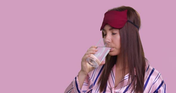 Woman Drinks From Glass of Crystal Clear Water in Pajamas and Sleeping Mask