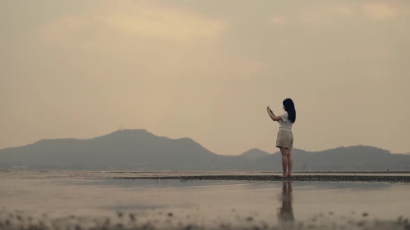 Asian woman taking a smartphone photo of sunset over the mountain.