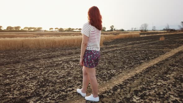 Young Farmer Woman Walks in an Arid and Burnt Field of Wheat