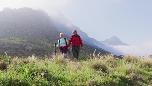 Senior hiker couple with backpacks and hiking poles holding hands and walking while hiking