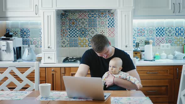 Single Dad Working on a Laptop Computer with Baby