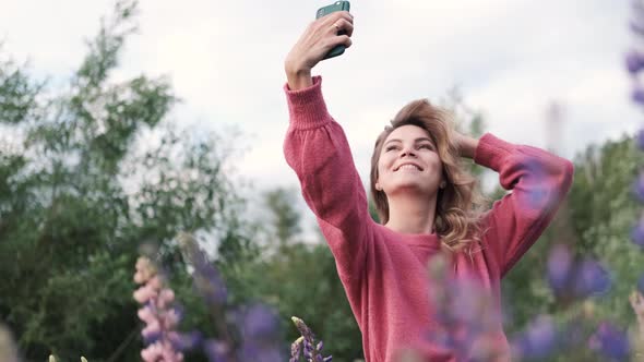 Happy Woman Enjoying Outdoors Taking Selfie Among Purple Lupine Flowers