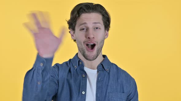 Young Man Waving and Welcoming on Yellow Background