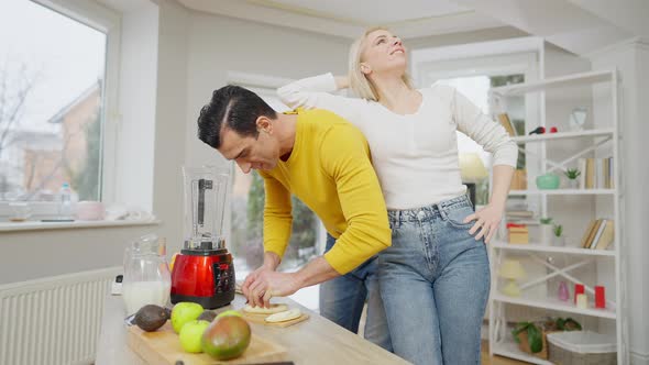 Cheerful Beautiful Woman Leaning on Man Cutting Banana for Healthful Dieting Smoothie