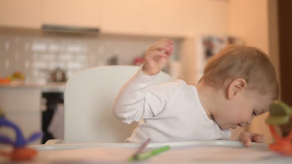 Little Cute Baby Toddler Boy Blonde Sitting on Baby Chair Learning Draw with Colour Pencils