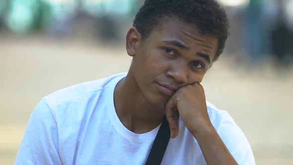 Confused African-American male teenager with arm sling outdoors