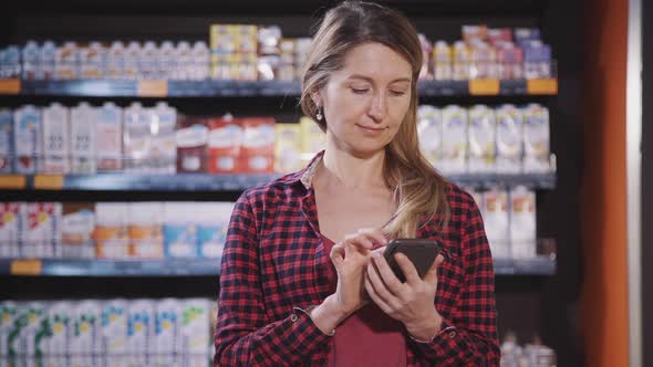 Woman Is Standing at Supermarket and Typing Message To Family Using and Holding New Portable Mobile