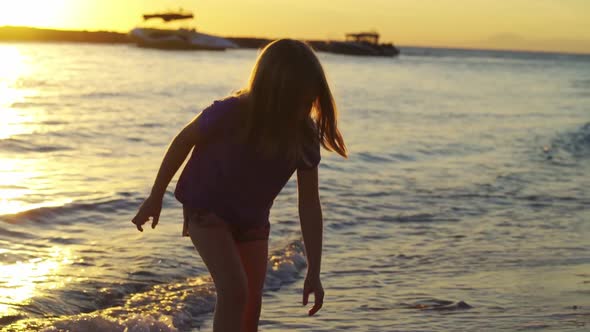 at Sunset Little Girl Walks Along Seashore and Throws Stones Into Water