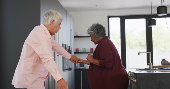 Happy senior diverse couple dancing in kitchen at retirement home