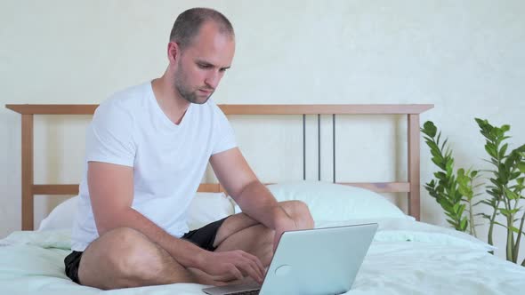 Man Is Working with a Laptop, Sitting on the Bed.