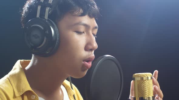 Young Asian Boy With Headphone Singing Into A Condenser Microphone On The Black Background