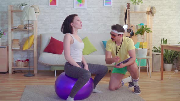 Funny Coach Man with a Mustache From the 80s Trains a Girl on a Fitness Ball in His House