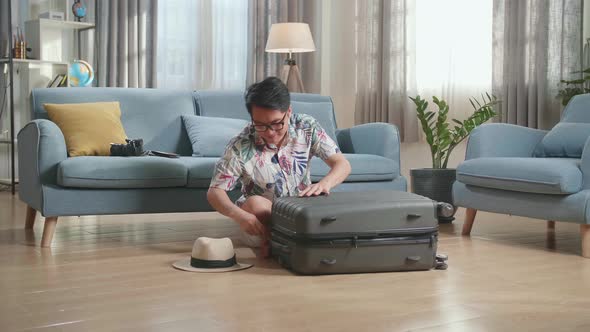 Asian Young Man Close Suitcase At Home, Preparing For Vacation