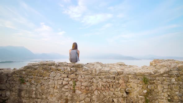 Girl Sitting on the Bricks Looks at the View to Lake Garda