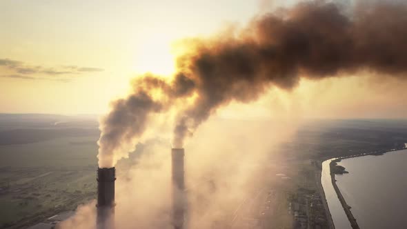 Aerial view of coal power plant high pipes with black smoke moving up polluting atmosphere at sunset alt