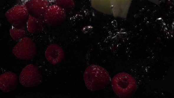 Raspberries, Blueberries, Blackberries and Apple Pieces Fall Into the Water on a Black Background