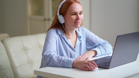Woman with Headphones Works at Home on a Laptop Leads a Lesson or Webinar