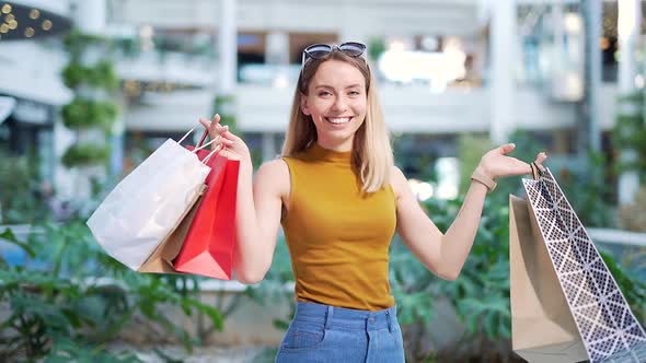 cheerful young shopaholic woman holding paper bags with purchases and smiling looking at camera 