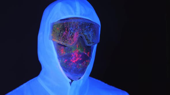 A Male in a White Luminous Suit Mask Splattered with UV Paint in the Dark