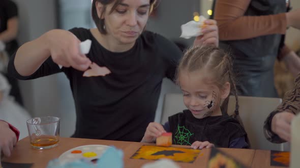 Little Girl Dressed Halloween Carnival Costume with Her Mother Sitting on the Table Drawing Handmade