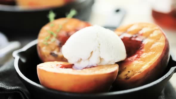 Organic grilled peaches with scoop of vanilla ice cream on a cast iron frying pan.