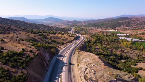 Aerial View of Cars Driving Down the Country Road Through Hills and Mountain