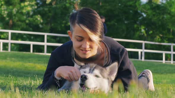 Beautiful Young Woman Playing with Funny Husky Dog Outdoors in Park